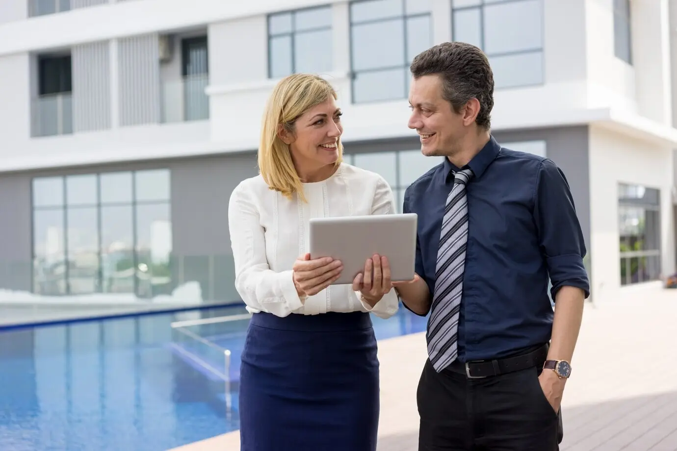 Счастливые бизнес‑партнёры читают новости на планшетном компьютере на открытом воздухе.